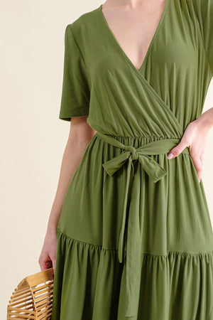 Close-up of a woman in a green soft short sleeve tiered midi dress, featuring a wrap bodice and tied waist detail.