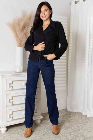 Woman modeling a stylish black zip-up jacket with pockets and dark blue jeans.