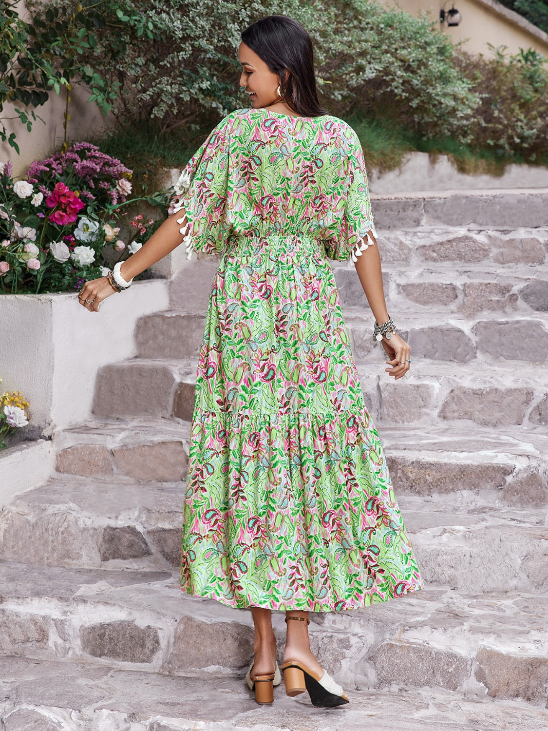 Back view of a woman in a floral V-neck short sleeve dress, styled with a flowy silhouette, walking down stone steps.