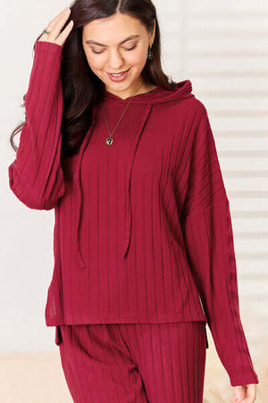 Cozy woman in burgundy ribbed hoodie with drawstring, part of matching two-piece pants set.