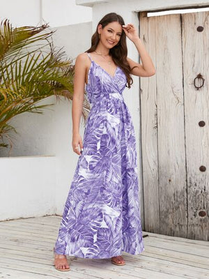 Woman in a purple printed surplice spaghetti strap dress, posing outdoors with palm leaves in the background.
