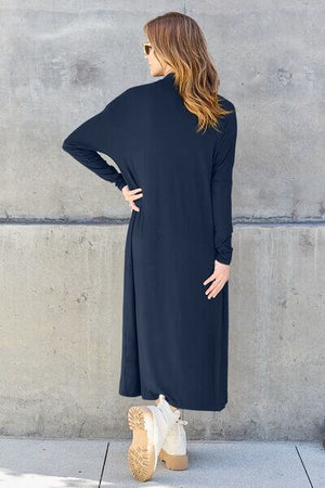 Back view of a woman wearing the Basic Bae Full Size Open Front Long Sleeve Cover Up in black against a concrete wall.