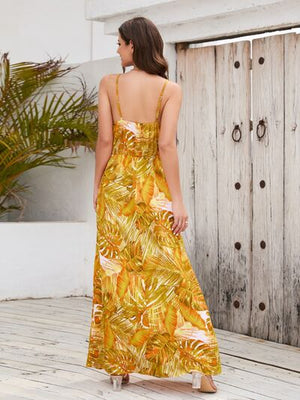 Stylish woman in a printed surplice spaghetti strap dress featuring a tropical leaf pattern, showcased against a rustic backdrop.