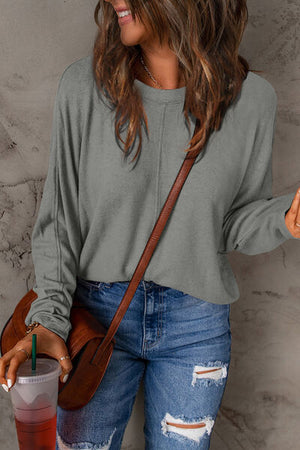 Woman wearing a gray long sleeve t-shirt with a stylish shoulder bag and jeans, enjoying a drink.