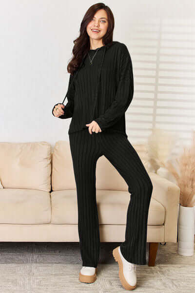 Model wearing a black ribbed hood top and pants set, showcasing cozy chic style in a modern living room.