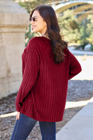 Women’s burgundy ribbed long sleeve knit top, showing back view, styled with sunglasses outdoors.