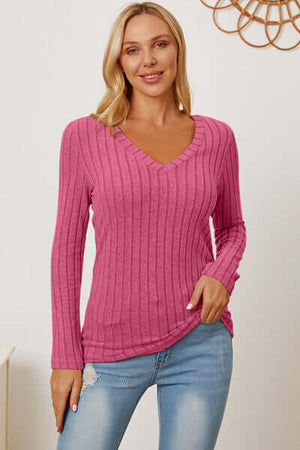 Woman wearing a pink ribbed V-neck long sleeve t-shirt, styled with light blue jeans.