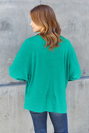 Woman in a green oversized top, showcasing a relaxed fit and stylish back view against a concrete wall.
