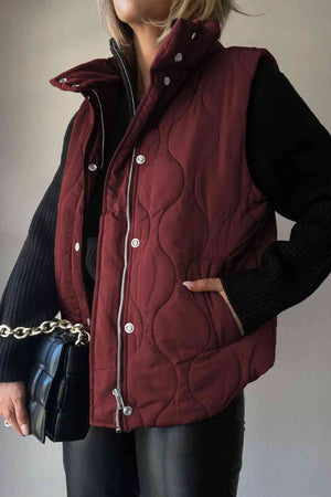 Model wearing a burgundy collared neck vest with pockets, styled with a black sweater and handbag.