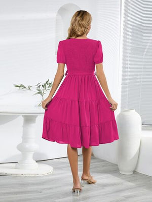 Back view of a model wearing a smocked tie front short sleeve tiered dress in vibrant pink, showcasing its flowing design.