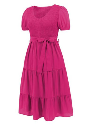 Smocked tie front short sleeve tiered dress in vibrant pink with a flowing design and bow detail.