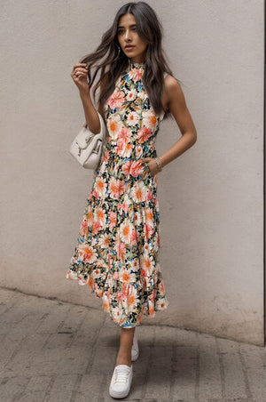 Model wearing a printed tiered pocketed mock neck midi dress with floral pattern and white sneakers.