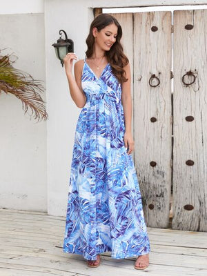 Model wearing a printed surplice spaghetti strap dress with blue tropical pattern, set against a rustic backdrop.