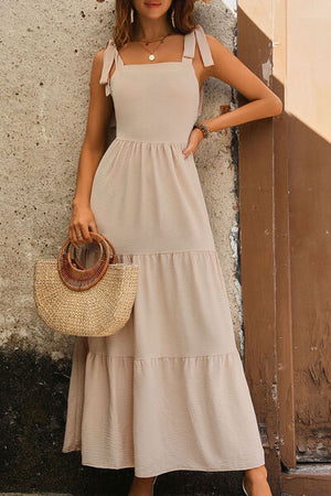 Woman wearing a tie shoulder smocked tiered dress, perfect for summer outings, paired with a stylish straw bag.