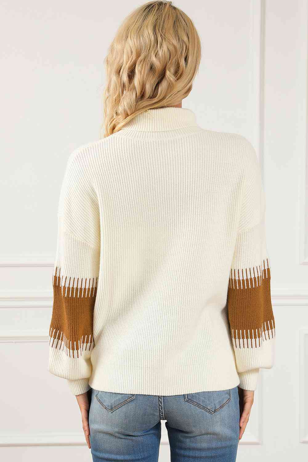 Back view of a contrast turtleneck long sleeve sweater featuring warm-colored sleeves, styled with jeans.