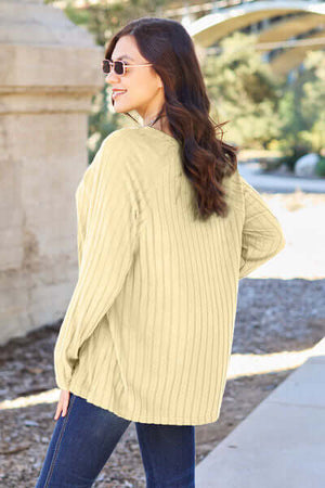 Woman wearing a light green ribbed knit top, showcasing a relaxed style and scenic outdoor background.