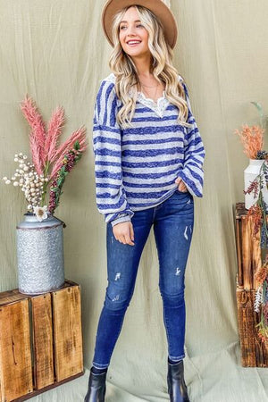 Woman in striped lace detail V neck top and jeans, smiling against a boho backdrop with plants and rustic decor.