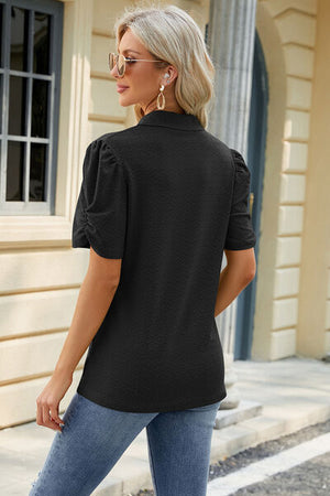 Woman wearing a black eyelet blouse with puff sleeves, styled with jeans and sunglasses.