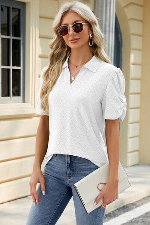 Stylish woman in eyelet white blouse with puff sleeves, sunglasses, and jeans, posing outdoors.