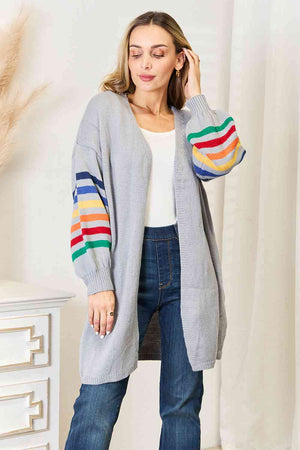 Model wearing a multicolored stripe open front longline cardigan over a white top and jeans, showcasing vibrant fashion.