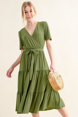 Model wearing a green tiered midi dress with short sleeves, holding a straw bag, showcasing effortless style.