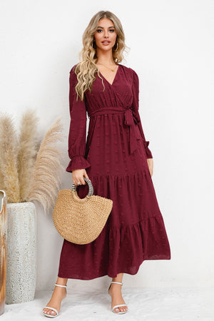 Elegant burgundy Swiss dot tied surplice flounce sleeve dress styled with a straw bag, perfect for any occasion.