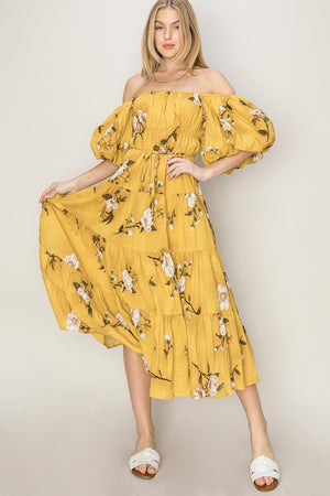 Model wearing a yellow floral puff sleeve tiered dress, featuring off-shoulder design and flowy skirt, perfect for any occasion.