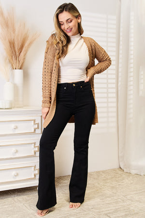 Stylish woman in a beige openwork ribbed cardigan, paired with black flared jeans, showcasing a trendy outfit.