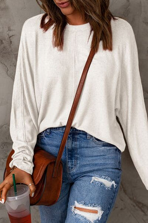 Woman wearing a casual white long sleeve t-shirt with jeans and a brown bag.