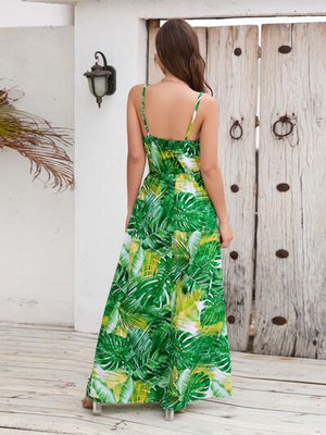 Back view of a woman wearing a green printed surplice spaghetti strap dress with tropical leaf patterns.