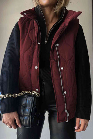 Stylish woman wearing a burgundy collared neck vest with pockets, paired with a black sweater and holding a chic handbag.