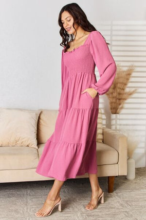 Woman in pink Culture Code ruffle trim smocked tiered dress with pockets, sitting on a sofa.