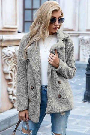 Woman wearing a full size lapel collar sherpa coat in gray, styled casually with jeans and sunglasses.