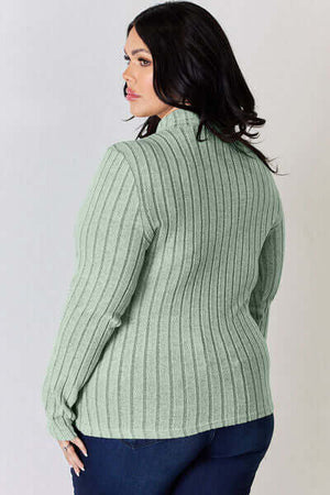 Back view of a plus-size woman wearing a ribbed mock neck long sleeve t-shirt in soft green.
