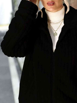 Woman wearing a black zip-up collared ribbed jacket over a white turtleneck.