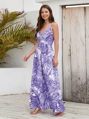Model wearing a purple printed surplice spaghetti strap dress, featuring a tropical leaf design, styled with a natural background.