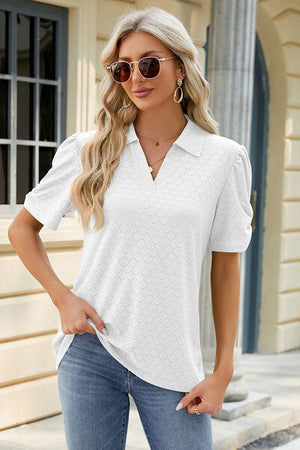 Woman in a white eyelet Johnny collar puff sleeve blouse with sunglasses, styled with jeans against a building backdrop.