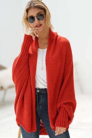 Woman wearing a longline open front ribbed cardigan in red paired with sunglasses and casual outfit.