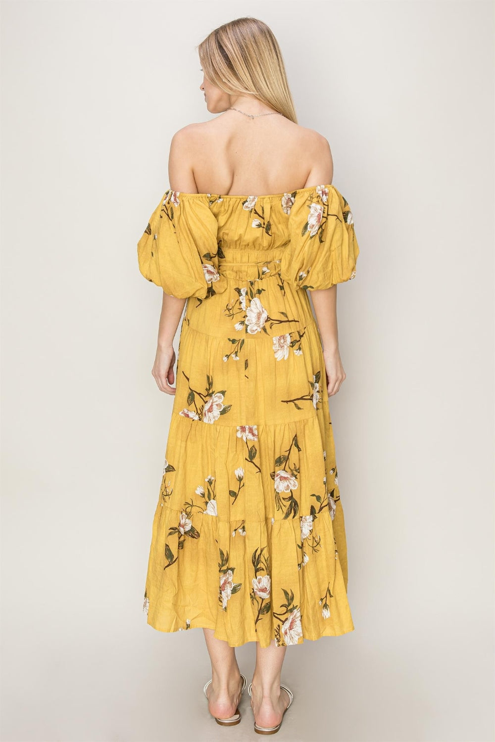 Back view of a woman wearing a yellow floral puff sleeve tiered dress, showcasing its romantic design.