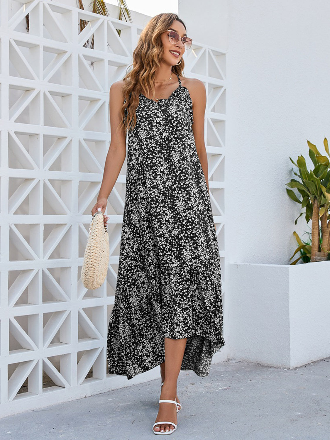 Elegant woman in a Ditsy Floral Scoop Neck Midi Cami Dress, styled with a bag and sunglasses, by a white wall.