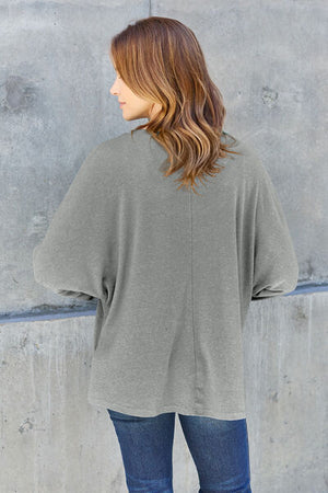 Woman wearing a casual gray oversized t-shirt, viewed from the back, standing against a concrete wall.
