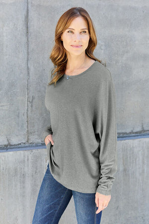 Model wearing a relaxed-fit long sleeve round neck t-shirt in olive green against a concrete wall.
