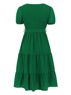 Back view of a green smocked tie front short sleeve tiered dress with puff sleeves.