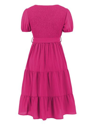 Back view of a pink smocked tie front short sleeve tiered dress with a flared skirt.