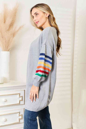 Side view of a woman wearing a gray longline cardigan with multicolored striped sleeves, styled with blue jeans.