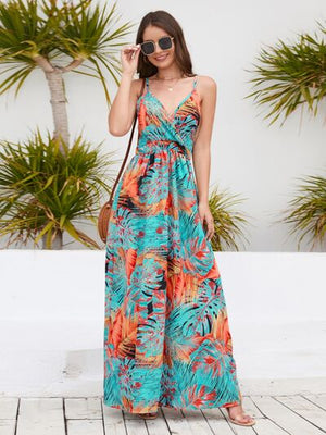 Woman modeling a colorful printed surplice spaghetti strap dress against a tropical background.