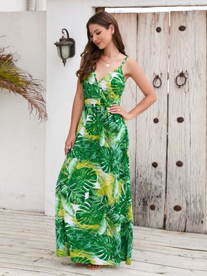Model wearing a printed surplice spaghetti strap dress with a green tropical leaf design in an outdoor setting.