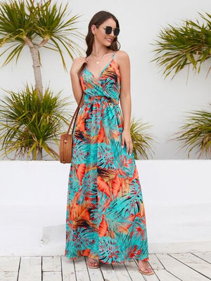 Model wearing a vibrant printed surplice spaghetti strap dress against tropical backdrop.