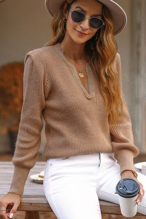 Stylish woman wearing a notched long sleeve sweater in beige with white jeans, holding a coffee cup.