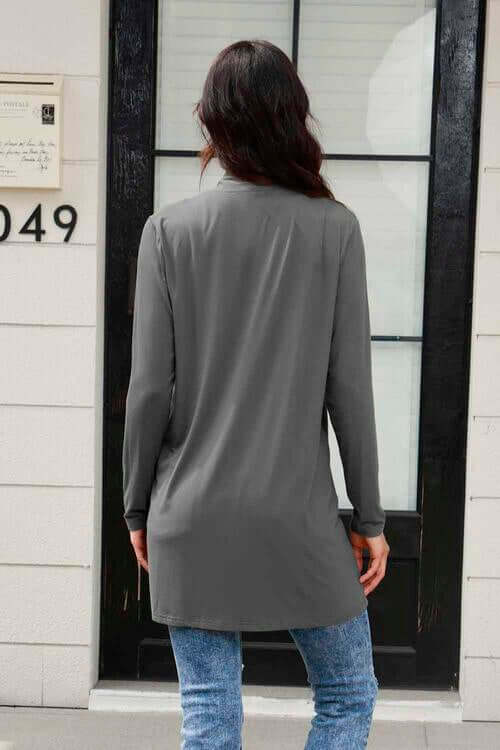 Back view of a woman wearing a gray long sleeve cardigan with pockets, paired with blue jeans.